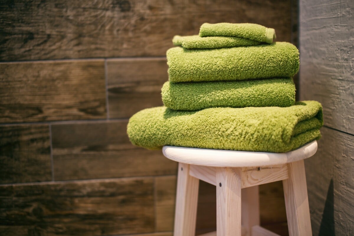 Picture of green folded towels on a white stool in a corner of a wood paneled room
